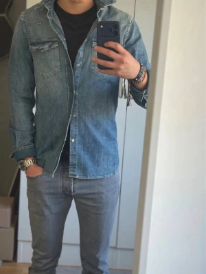 Dondup skjorta - Säljer en klassisk blå jeansskjorta med långa ärmar och tryckknappar framtill. Skjortan har två bröstfickor med lock och en avslappnad passform. Perfekt att styla lager på lager eller bära som den är. Pris kan diskuteras 