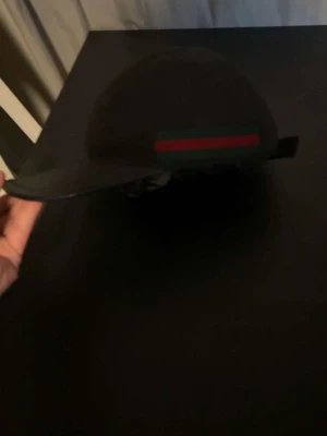 Gucci keps (äkta) - Snygg svart keps med rak skärm och en tydlig röd och grön rand på sidan. Klassisk och stilren design som passar till många olika outfits. Justerbar baktill för bästa passform.