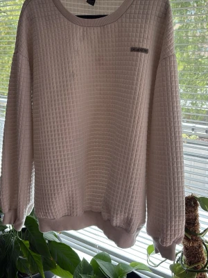 Ljusrosa sweatshirt från SHEIN - Ljusrosa sweatshirt från SHEIN med rutmönstrad struktur. Tröjan har rund halsringning, ribbade muddar vid ärmslut och nederkant samt en liten logga på bröstet. Perfekt för en avslappnad och trendig look.
