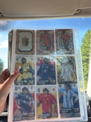Flera fotbolls kort och en map till  - Samling av Panini fotbollssamlarkort i plastficka, med färgglada motiv av olika internationella spelare och specialkort. Korten har olika färger, siffror och grafik, och är tillverkade i glansig kartong. Perfekt för dig som gillar att samla på sportkort.