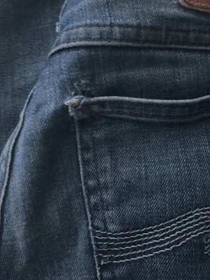 Mörkblå jeans från Nudie Jeans - Snygga mörkblå jeans från Nudie Jeans med klassisk femficksmodell och kontrastsömmar på bakfickan. Jeansen har en skön passform och är tillverkade i slitstarkt denimtyg. Perfekta för dig som gillar en tidlös och avslappnad stil.
