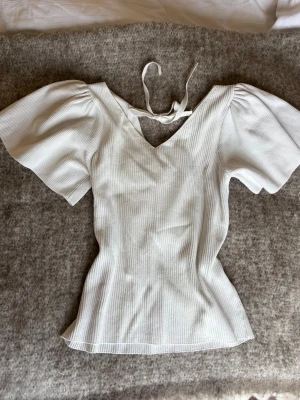 Vit ribbad topp med puffärm och knyt - Jättefin topp med knyte i ryggen, det är mammas och tyvärr så är lappen på den borta så vet inte storlek men skulle säga främst storlek M eller S. ☺️