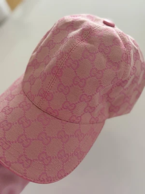 Rosa keps GG - Helt ny och oanvänd med lapp kvar. Säljer en snygg rosa keps med klassiskt GG-monogram i ton-i-ton rosa. Kepsen har böjd skärm och justerbar rem bak i matchande färg. Tillverkad i slitstarkt tyg som ger en exklusiv känsla och look.