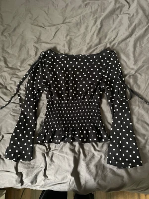 Svart prickig blus  - Säljer en svart blus med vita prickar och långa ärmar. Toppen har snörning på axlarna, smockad midja och lätt utsvängd nederkant. Aldrig använd, endast provad💓