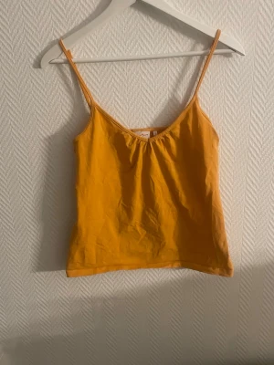 Orange linnetopp med smala axelband - Snygg orange linnetopp med smala axelband och v-ringning. Perfekt till sommaren och enkel att matcha med jeans eller kjol. Tillverkad i mjuk bomull som känns skön mot huden.