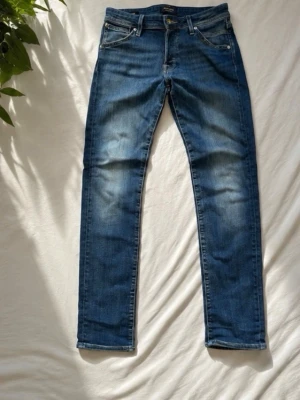 Jack & Jones jeans - Snygga blå slim fit jeans med lätt slitna detaljer på låren och knäna. Klassisk femficksmodell med dragkedja och knapp i midjan. Jeansen har en modern passform och är perfekta för en avslappnad stil.