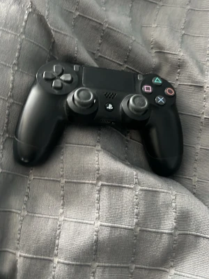 Svart PlayStation DualShock 4 kontroll - En svart PlayStation DualShock 4 handkontroll med klassisk layout, touchpad och färgade symbolknappar. Ergonomisk form och tillverkad i plast, perfekt för gaming på PS4. USB-port och inbyggd högtalare för extra funktionalitet.