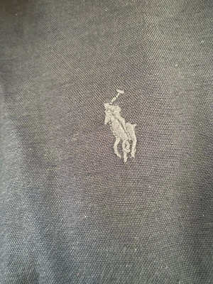 Mörkblå skjorta från Polo Ralph Lauren - Snygg mörkblå skjorta från Polo Ralph Lauren med klassisk broderad logga på bröstet. Skjortan är tillverkad i bomull och har en tidlös design som passar perfekt till många olika stilar.