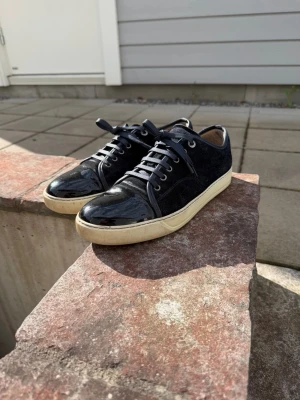 Marinblå Lanvin sneakers i mocka och lack - Snygga svarta sneakers från Lanvin med ovandel i mocka och lackdetaljer på tån och runt snörningen. Skorna har vita sulor och klassisk låg profil. Perfekta för dig som vill ha en stilren och exklusiv look. Levereras med originalkartong och dustbag.