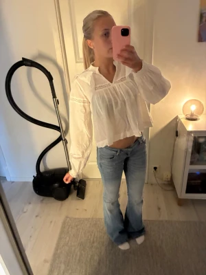 Vit blus med spetsdetaljer - Säljer en luftig vit blus med långa ärmar och fina spetsdetaljer vid bröstet och ryggen. Blusen har en lös passform, v-ringad hals och volangkant nedtill. Perfekt för en trendig och avslappnad look.