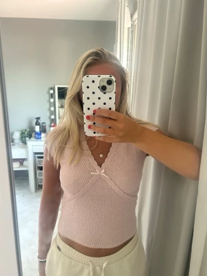 Ljusrosa ribbad croppad topp med rosett - Supersöt ljusrosa croppad topp med ribbad struktur och liten rosett framtill. Toppen har v-ringning och är ärmlös, perfekt för varma dagar. Söt och feminin stil som passar till många outfits.