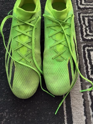 Gröna Adidas fotbollsskor - Snygga gröna fotbollsskor från Adidas med svarta detaljer och klassiska ränder på sidorna. Skorna har snörning och ovandel i mesh-liknande syntetmaterial som ger bra ventilation och passform. Perfekta för dig som vill sticka ut på planen.