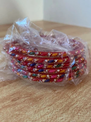 Röda bangles från Indien  - Armbanden har en rund form och glittriga detaljer som ger en lekfull och trendig vibe. Perfekt för att addera färg till din outfit! Köpt från Indien! 
