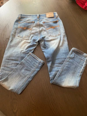 Blå slim fit jeans med slitningar - Säljer ett par blå slim fit jeans med snygga slitningar och ljusa tvättade partier. Jeansen har klassiska fem fickor och kontrastsömmar på bakfickorna. Materialet är mjukt denim som sitter skönt och följer kroppen.