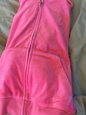 Rosa zip hoodie med huva - Säljer en riktigt snygg rosa hoodie med dragkedja och stor ficka framtill. Hoodien har en huva och är gjord i mjukt, fleeceliknande material som känns skönt mot huden. Perfekt för dig som gillar färgstarka plagg och vill sticka ut lite extra.