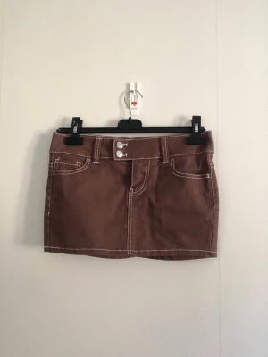 Brun kortkjol med kontrastsömmar - Jättesnygg brun kortkjol med vita kontrastsömmar och dubbla knappar framtill. Prislappen kvar, kostar originalt 200kr. Pris kan diskuteras 💕