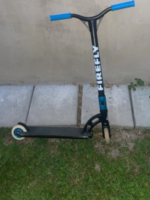 Svart trick sparkcykel Firefly - Säljer en svart trick sparkcykel från Firefly med blåa handtag och detaljer. Styret är i metall och däcken är små och slitstarka, perfekta för skateparken. Snygg design med vit logga på styret och robust konstruktion för tricks och hopp.