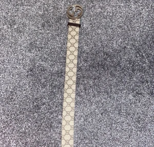 Beige GG-bälte från Gucci - Snyggt beige bälte från Gucci med det klassiska GG-mönstret och en silverfärgad GG-spänne. Bältet är gjort i skinn och har en exklusiv känsla som lyfter vilken outfit som helst. Har kvitto 