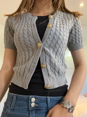 Grå kortärmad kofta - Kortärmad kofta med dekorativa guldknappar framtill. 🤍Perfekt att styla över ett linne eller t-shirt för en trendig look🤍