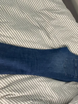 Blå bootcut jeans med klassisk tvätt - Säljer ett par blå bootcut jeans med klassisk tvätt och femficksdesign. Jeansen har en knappstängning och dragkedja framtill samt snygga detaljer på bakfickorna. Perfekta för dig som gillar en tidlös och avslappnad look.