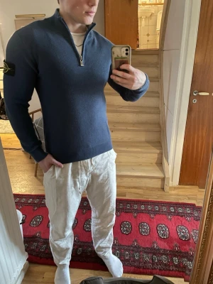 Blå quarter-zip från Stone Island - Snygg blå tröja från Stone Island med halv dragkedja och ribbad struktur. Tröjan har lång ärm och ikonisk logopatch på vänster ärm. Perfekt för dig som gillar stilrena och exklusiva plagg.