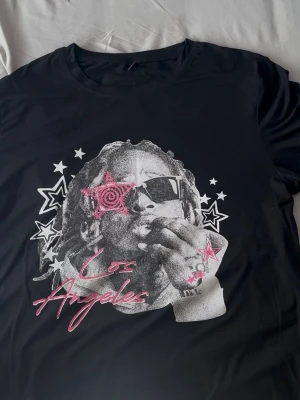 Svart t-shirt med Los Angeles-tryck - Cool svart t-shirt med tryck av Los Angeles i rosa text och grafiskt motiv med stjärnor på framsidan. T-shirten har rund hals och korta ärmar, perfekt för en avslappnad streetstyle-look.
