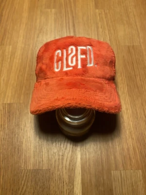 Röd keps från Classified - Säljer en röd keps från Classified med broderad vit logga framtill. Kepsen har en mjuk, nästan plyschliknande yta och justerbar snapback baktill. Insidan har meshpaneler för extra ventilation. Perfekt för dig som vill sticka ut med en unik accessoar.