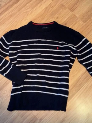 Marinblå randig tröja Polo Ralph Lauren - Öppen för prisförslag. Snygg marinblå stickad tröja från Polo Ralph Lauren med vita horisontella ränder och röd broderad logga på bröstet. Tröjan har rund halsringning och ribbade muddar vid ärmslut och nederkant. Perfekt för en klassisk och avslappnad stil.