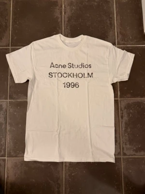 Acne studios t shirt - Riktigt fet och eftertraktad t-shirt med acne studios loggan i storlek M. Väldigt bra skick!  Obs: Jag är lite osäker på äktheten då lappen i nacken saknas, därför säljs den billigare (499 kr, nypris ca 3000 kr).  längd cirka 67cm, bredd cirka 47cm. Tveka inte att höra av dig vid frågor eller funderingar!