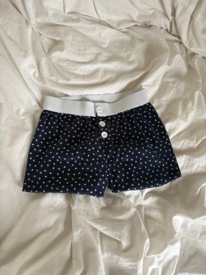 Mörkblå pyjamasshorts - Snygga mörkblå pyjamasshorts med små vita blommönster och bred vit resår i midjan. Oanvända då dom var fel storlek. 