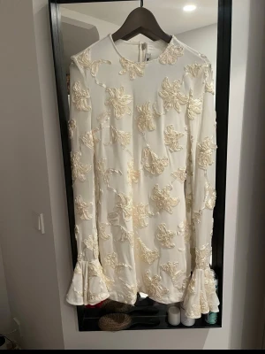 Vit studentklänning med spetsdetaljer - Supersnygg vit kortklänning som passar perfekt till studenten. Klänningar har blommor och långa ärmar med volang vid ärmslut. Använd en gång på min student😊😊nypris ca 3000