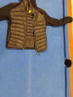 Svart pufferjacka från Parajumpers - Säljer en svart pufferjacka från Parajumpers med quiltad front, stickade ärmar och axlar samt dragkedja. Jackan har en gul detalj vid halsen och innerficka med dragkedja. Perfekt för kalla vinterdagar och riktigt snygg streetstil. Den här helt ny och äkta 