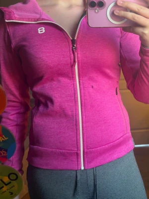 Rosa tränings zip-hoodie från 8848 - Snygg rosa zip-hoodie från märket 8848 med vit dragkedja och liten logga på bröstet, tänkt för träning/gym. Tröjan har huva, långa ärmar och två sidofickor med dragkedja. Perfekt för träning eller chill. Materialet är mjukt och stretchigt för skön passform.