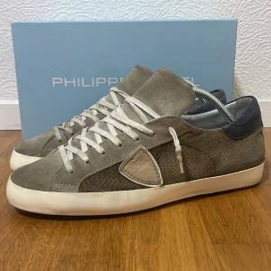Grå sneakers från Philippe Model - Snygga grå sneakers från Philippe Model med vita snören och vit sula. Skorna har en mix av mocka och skinn, samt en mörkare grå hälkappa. Klassisk rund tå och diskret logodetalj på sidan. Storlek 43 passar också storlek 44. Dessa skor är Limited edition och tillverkas ej längre och nypris ligger runt 5000 kr när dem såldes. Önskas fler bilder så är det bara att skriva! 💬 Jag köpte skorna för användning under sommarn men kan inte använda dom längre i och med att jag bröt foten.