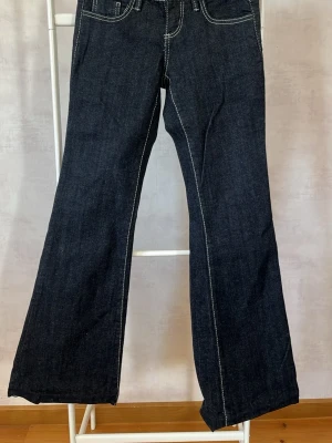 Mörkblå bootcut jeans med kontrastsömmar - Snygga mörkblå bootcut jeans med vita kontrastsömmar och klassisk femficksmodell. Jeansen har utsvängda ben, perfekta för en trendig och avslappnad look. Tillverkade i kraftigt denimtyg som ger en schysst passform. (Aldrig använda men saknar prislapp och är lite avklippta)