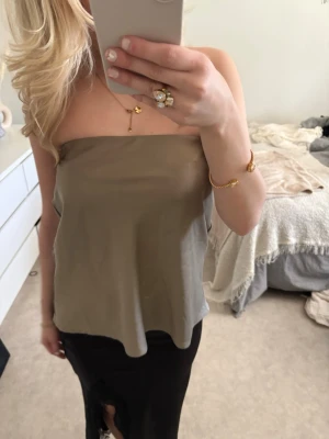 Beige axelbandslös tubtopp - Snygg beige axelbandslös tubtopp i ett mjukt och lätt material. Toppen har en enkel och stilren design med rak skärning upptill och faller löst över kroppen. Perfekt för varma dagar eller att styla med smycken.