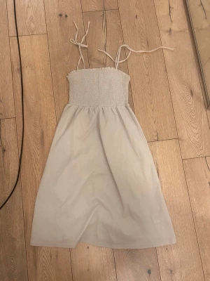 Två vita sommarklänningar - Säljer två vita klänningar, en med smock upptill och knytband samt en kortärmad med knappar framtill. Perfekta för varma dagar och har en luftig passform. Båda är i lätt material och passar dig som gillar enkel och stilren design.