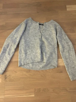Ljusgrå kofta med knappar - Mysig ljusgrå kofta med rund halsringning och tre knappar framtill. Koftan har lång ärm och är stickad i ett mjukt material. Perfekt att slänga på sig när det är lite kyligt ute.