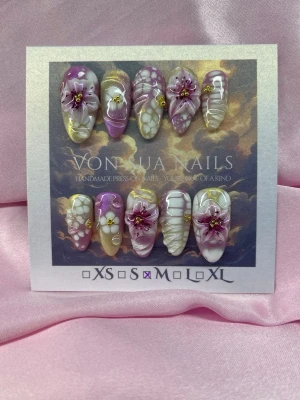 BloomGlitch (M);Medium Almond - Unika Handgjorda press-on naglar i storlek M: 16 mm, 12 mm, 12,5 mm, 11,5 mm, 10 mm. Naglarna har en lila och vit unik bas med 3D-blommor, gulddetaljer och pärlor. Formen är medium långa almond och designen är unik med både glansiga och matta inslag. Perfekt för dig som vill ha något extra.M: 16 mm, 12 mm, 12,5 mm, 11,5 mm, 10 mm, handgjorda blommor målade med airspray