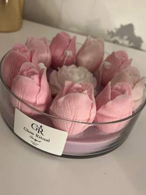 DoftLjus i glas med blomdesign Glow Ritual - Unikt doftljus från Glow Ritual i glasbehållare, dekorerat med rosa och vita blommor i vax. Ljuset har en rund form och blommorna är detaljerat utformade som tulpaner och en ros i mitten. Perfekt som dekoration eller present.