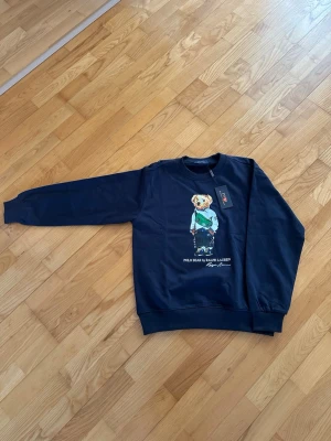 Mörkblå sweatshirt Polo Bear - mörkblå sweatshirt från Ralph Lauren med Polo Bear på bröstet. Tröjan har rund hals, ribbade muddar och är tillverkad i mjukt material. Perfekt för dig som gillar streetstyle och ikoniska prints. Skickas snabbt 📦