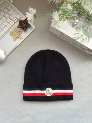 Moncler svart mössa med logga - Snygg svart ribbstickad mössa från Moncler med uppvikt kant. Mössan har en vit, röd och marinblå rand samt Monclers ikoniska logotyp framtill. Perfekt accessoar för att hålla värmen och addera stilpoäng till din outfit.