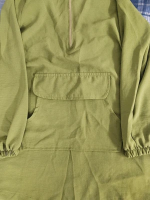 Olivgrön hoodie med dragkedja - Säljer en olivgrön hoodie med halv dragkedja framtill och stor magficka med lock. Tröjan har långa ärmar med resår vid ärmsluten och är tillverkad i ett mjukt bomullsliknande material. Perfekt för en avslappnad och chill stil.