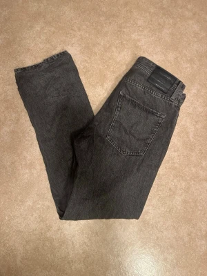 Svarta raka jeans från Jack & Jones - Snygga svarta jeans från Jack & Jones 30/32 med rak passform och klassisk femficksdesign. Jeansen har en mörkgrå tvätt och är tillverkade i ett robust bomullstyg. Perfekta för en stilren och avslappnad look.