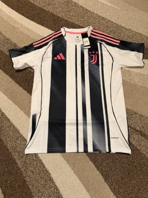 Juventus 25-26 Hemmatröja  - Säljs av ICEKIT  Storlek: M Namn + nummer: Inget Badge: Ingen  Här kan du se tröjor i ICEKIT Outlet. Alla tröjor är helt nya och utan några problem. Du kan välja att köpa dem här eller direkt via vår hemsida.  Tröjorna finns tillgängliga hos ICEKIT på: https://www.icekit.se  Länk: https://www.icekit.se/collections/outlet
