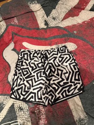 Svarta och vita shorts med grafiskt mönster - Snygga shorts med svartvitt grafiskt mönster och dragsko i midjan. Perfekta för sommaren och riktigt sköna att ha på sig. Materialet känns lätt och luftigt, perfekt för varma dagar.