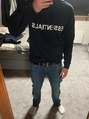 Mörkblå Essentials hoodie - Snygg mörkblå hoodie från Essentials med vit logga framtill. Perfekt för en chill och avslappnad stil. 100% polyester. Skriv vid frågor, jag svarar snabbt!