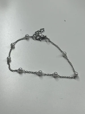 Silverfärgat armband med pärlor - Snyggt och stilrent armband i silverfärg med små vita pärlor jämnt fördelade längs den tunna kedjan. Perfekt för dig som gillar minimalistiska smycken med en elegant touch. Justerbart spänne för bästa passform. Går att flytta pärlorna, rostfritt. Köpt för 399kr