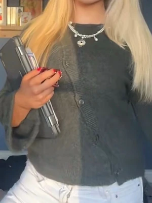 Mörkgrön kofta med sned knäppning - Mysig mörkgrön kofta med unik sned knäppning framtill och rund halsringning. Koftan har långa ärmar och är tillverkad i ett mjukt, fluffigt material som känns skönt mot huden. Perfekt att slänga på sig för en avslappnad och trendig look.