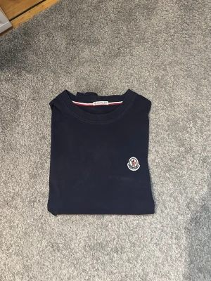 Mörkblå Moncler t-shirt i bomull - Snygg mörkblå t-shirt från Moncler med klassisk rund hals och diskret Moncler-logga på bröstet. Tillverkad i mjuk bomull som känns skön mot huden. Perfekt till jeans eller shorts för en clean och stilren look.